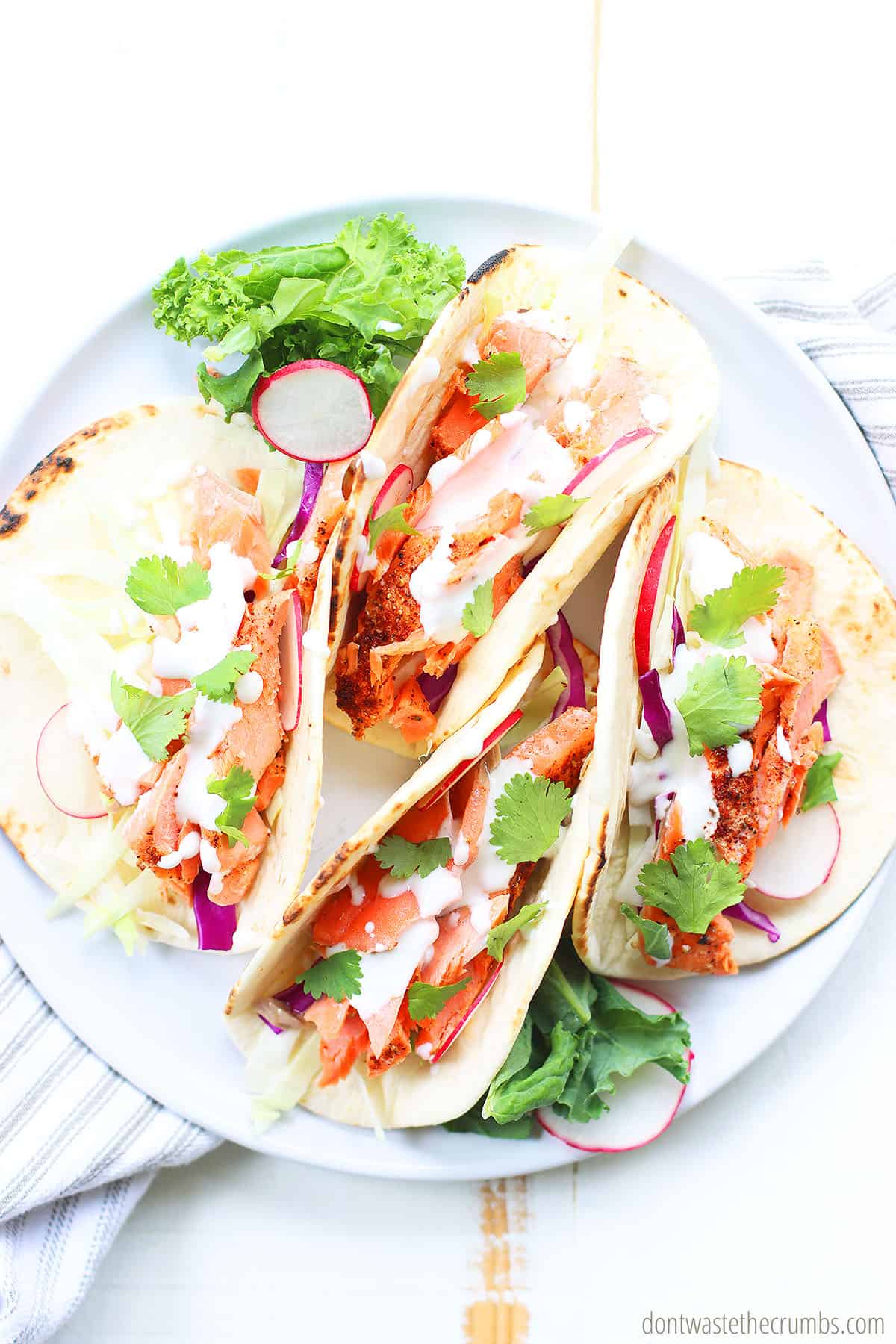 3 spicy salmon tacos on a white plate.