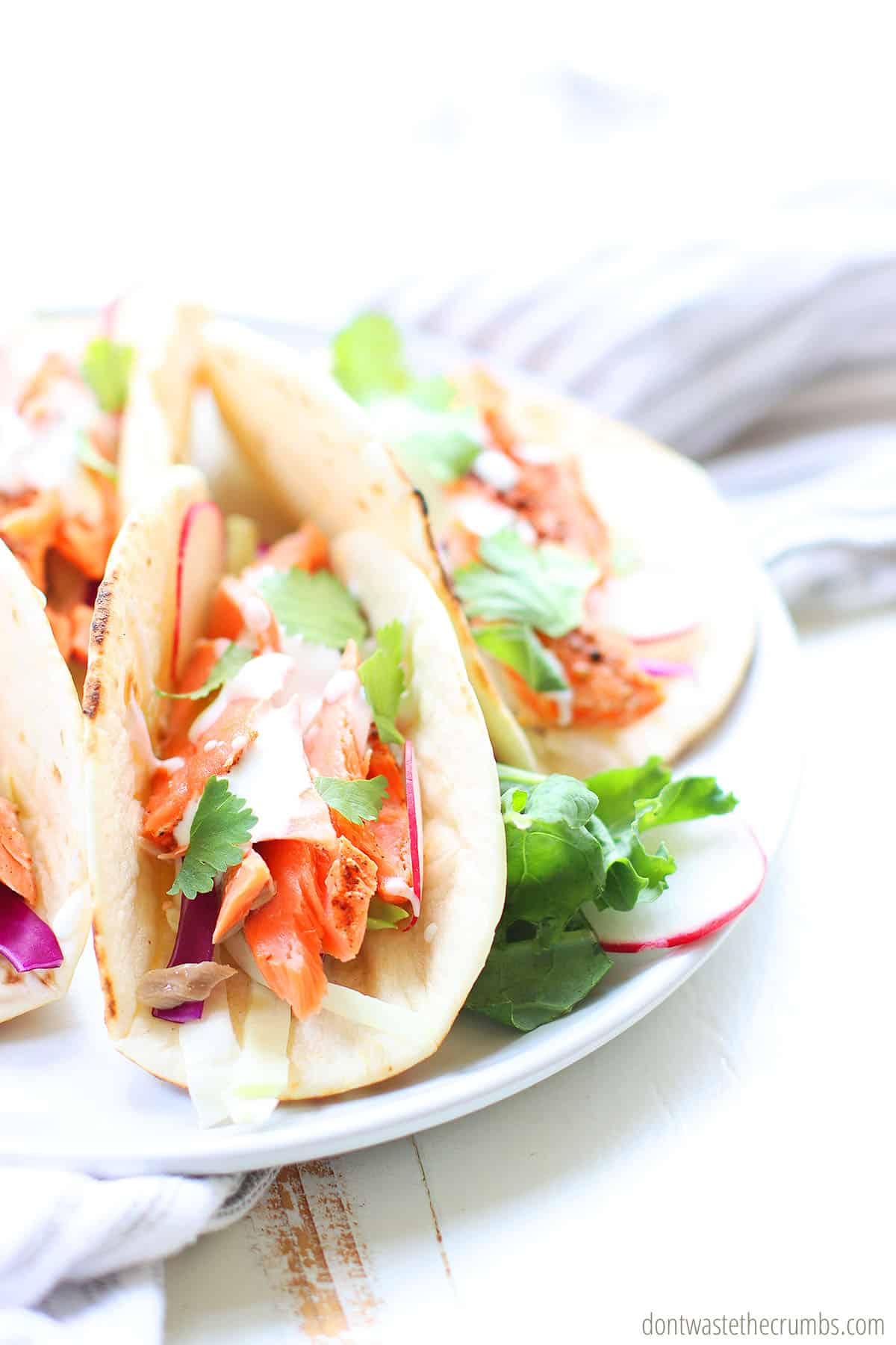 Spicy salmon tacos are on a white plate.