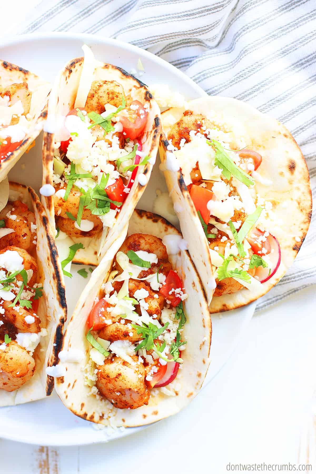 Five spicy shrimp tacos on a white plate