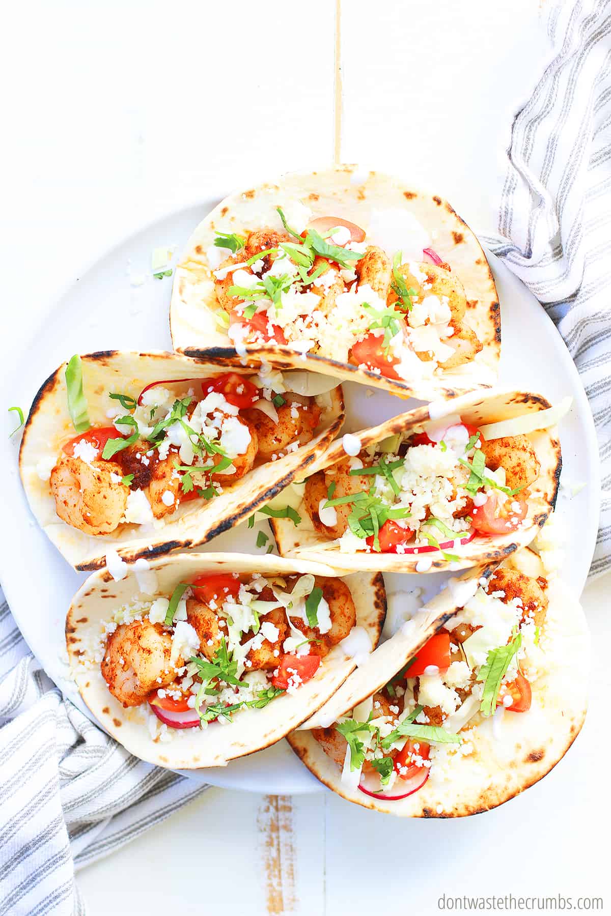 Five spicy shrimp tacos on a white plate