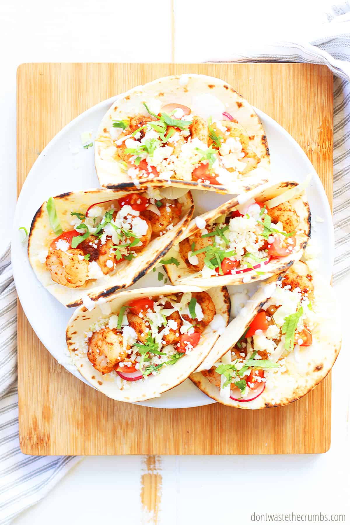 Five spicy shrimp tacos with creamy slaw on a plate on top of a wood cutting board
