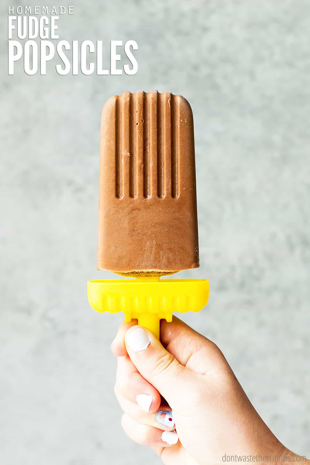 A child's hand holds a fudgesicle, with the text overlay that reads "Homemade Fudge Popsicles." They're simple, easy to make and healthier than store-bought. 