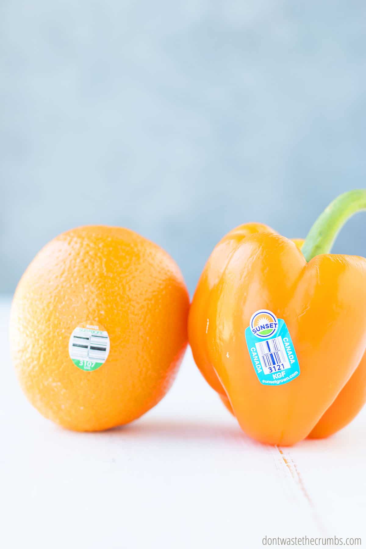 Orange and orange bell pepper on a table with PLU stickers.