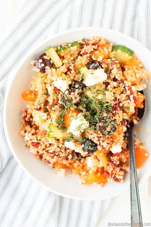 Greek quinoa salad in a white bowl with a spoon in it.