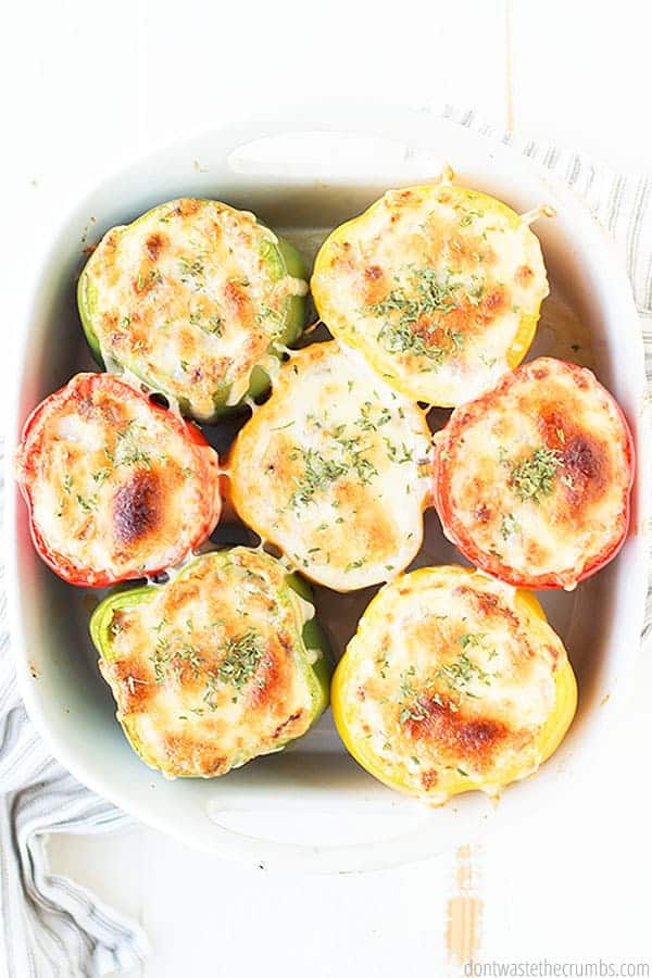 Seven stuffed bell peppers in a white baking dish.
