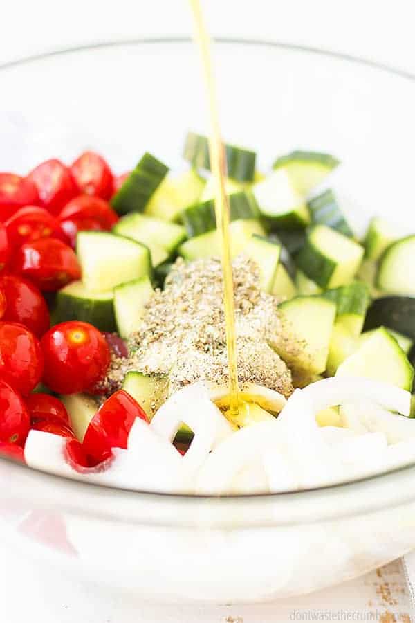 Vegetable Greek salad in a large bowl and homemade Greek salad dressing being poured over the vegetables.