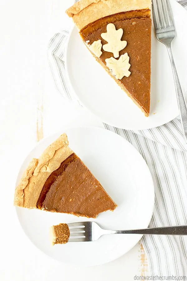 Two slices of pumpkin pie on their own white dish and forks.