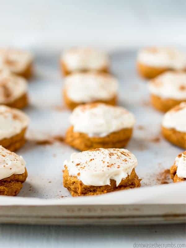 Pumpkin cookies with cream cheese frosting. All laid out on a baking sheet with parchment paper.