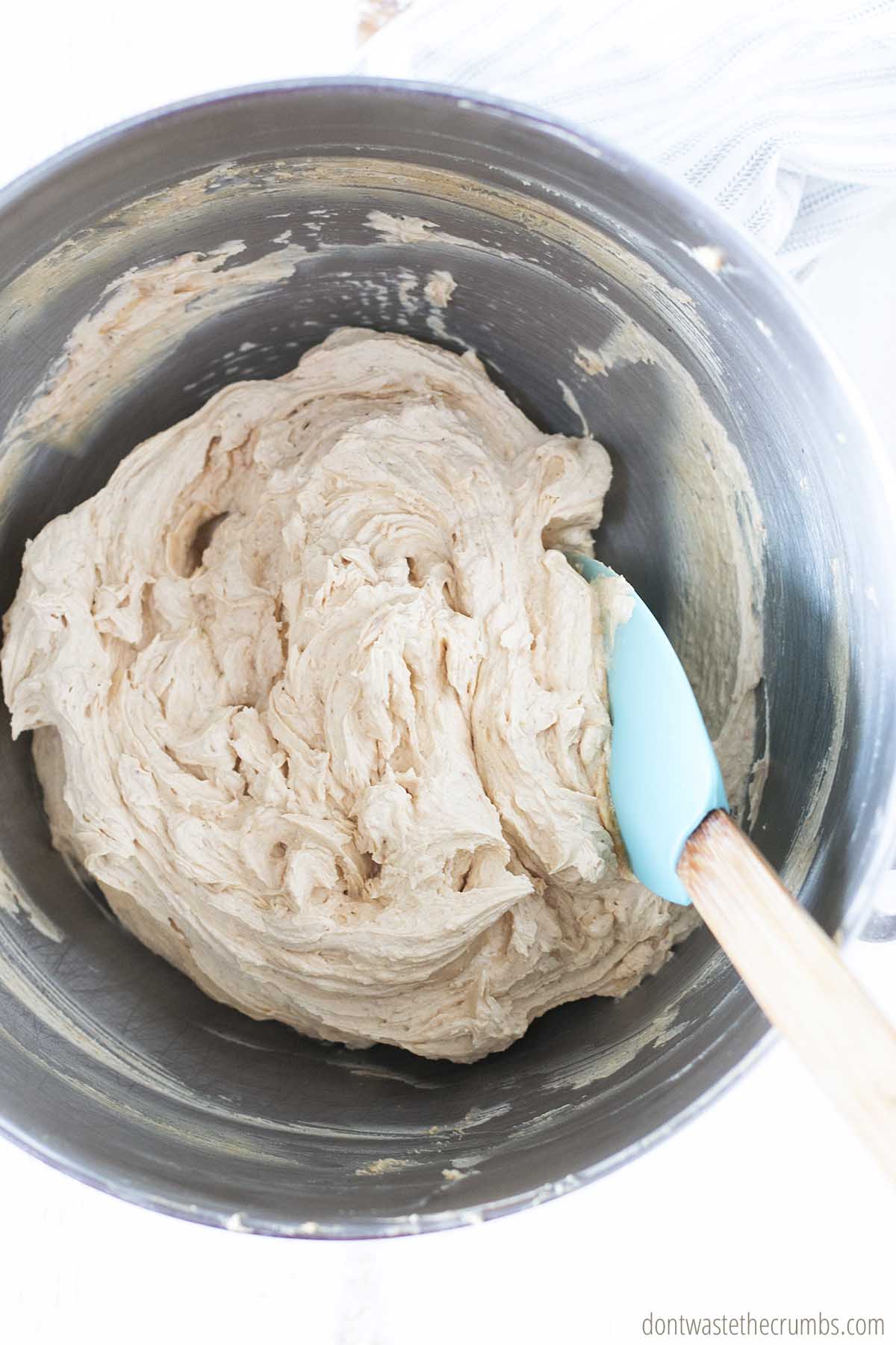 Homemade peanut butter frosting in a stainless steel mixing bowl, mixed with a spatula.
