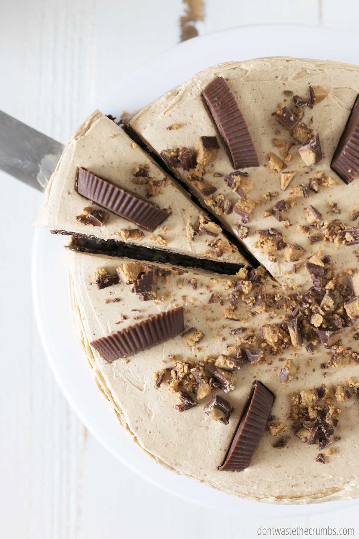 A wedge of chocolate peanut butter cake, topped with chopped peanut butter cups is being served.
