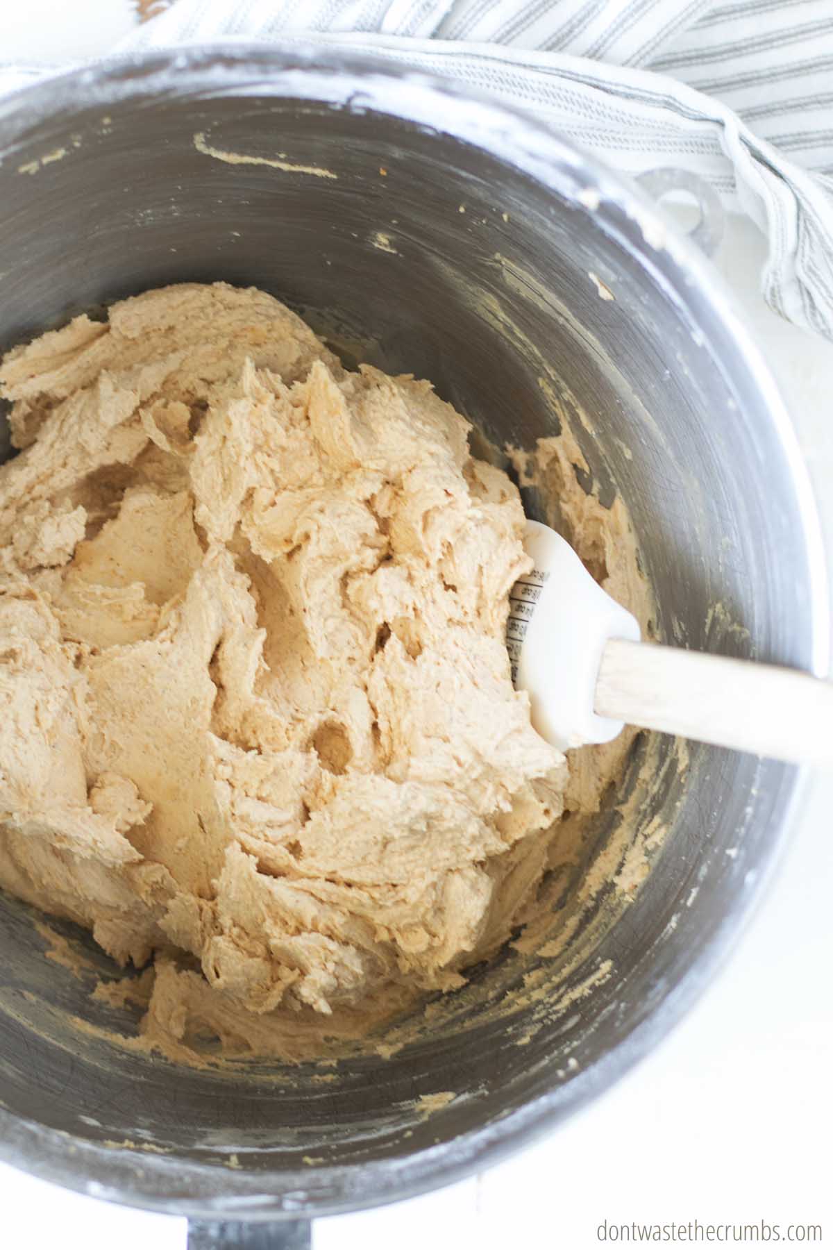 Silky peanut butter frosting is stirred with a with spatula inside a stand mixer.