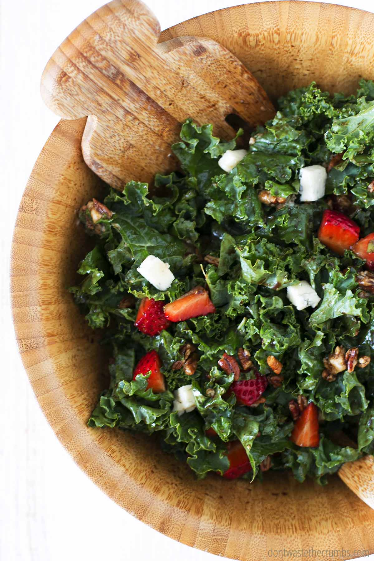 Kale salad recipe with strawberries, pecans and blue cheese in a wooden bowl, ready to be served.
