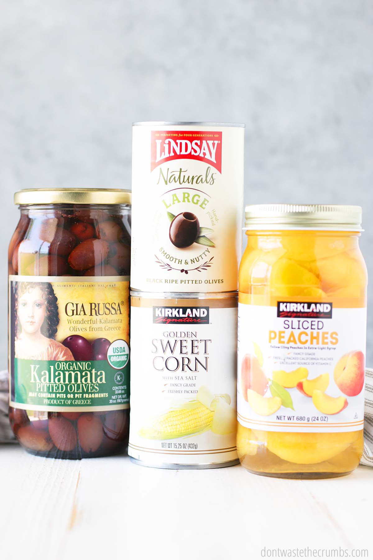 Pantry goods you can buy at Costco, including kalamata olives, canned olives, canned sweet corn, and a jar of peaches