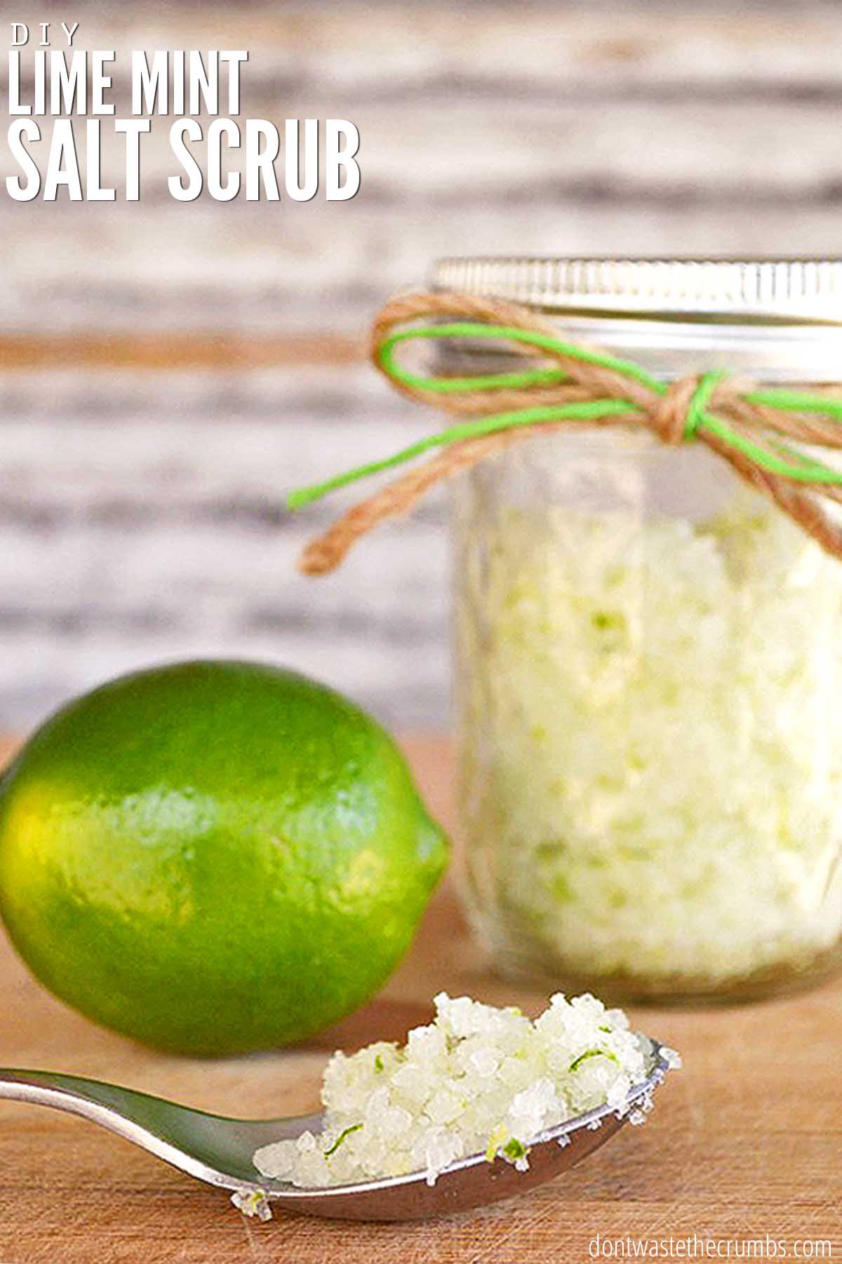 Spoonful of homemade body scrub and a lime nearby. There is a mason jar with lime mint salt scrub behind the spoon. Text overlay reads, "DIY Lime Mint Salt Scrub".
