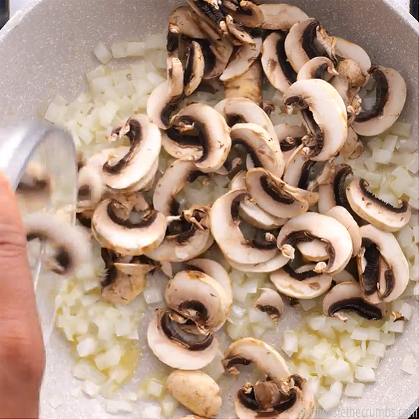 Chopped onions and mushrooms in a frying pan. Small bowl of rice being poured into the pan with the other ingredients.