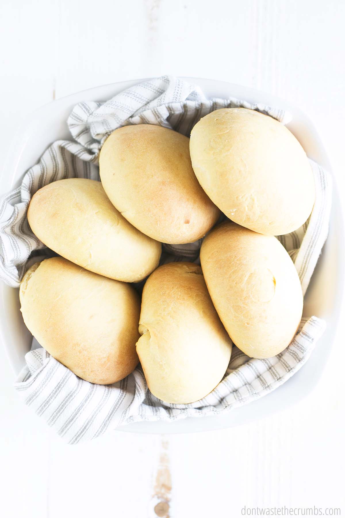 Six homemade hamburger buns in a large bowl lined with a cloth napkin.