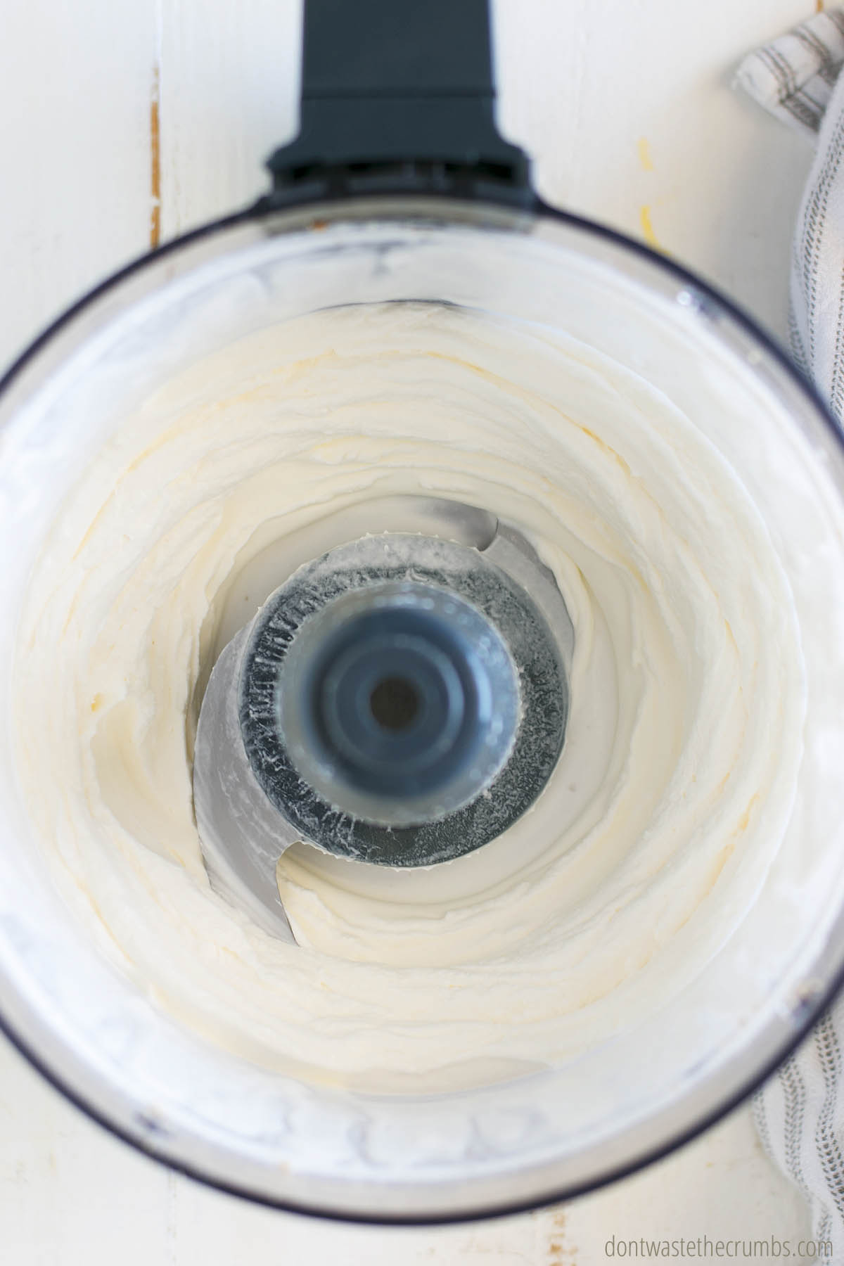 Heavy whipping cream and cream cheese being processed in a food processor with vanilla and maple syrup.