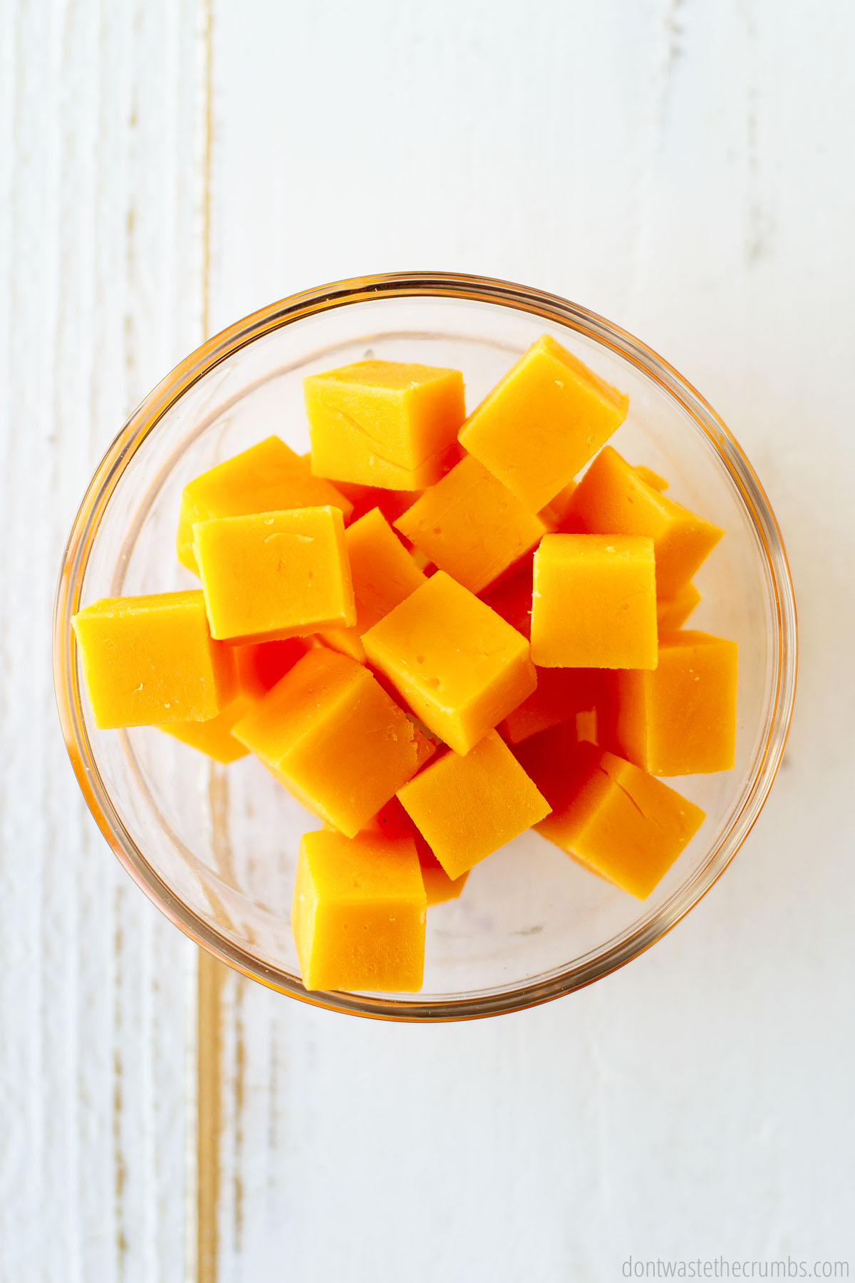 Cubes of cheddar cheese in a clear bowl.