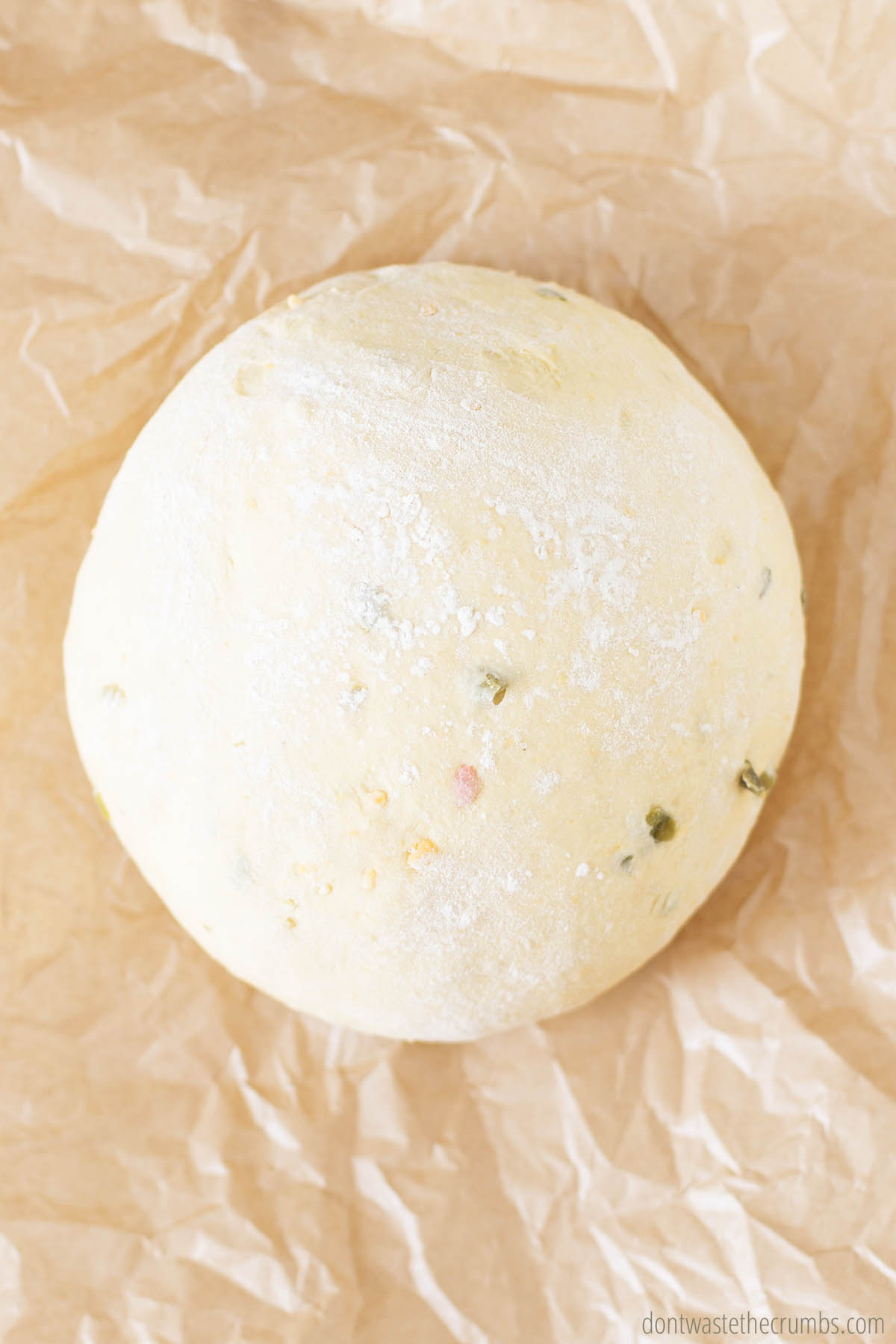 A ball of risen jalapeno cheddar bread dough on parchment paper.