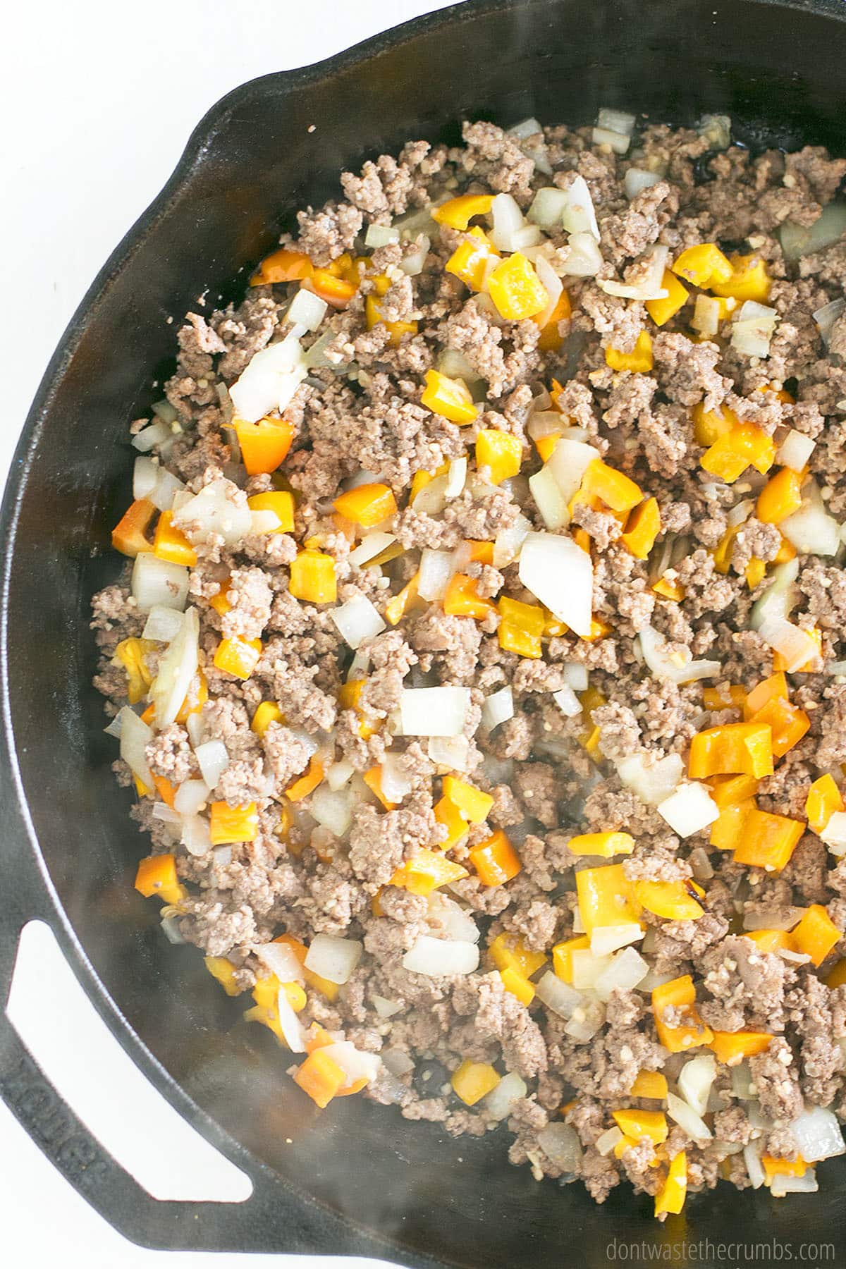 Ground beef and other ingredients for a beef tamale pie in a cast iron skillet
