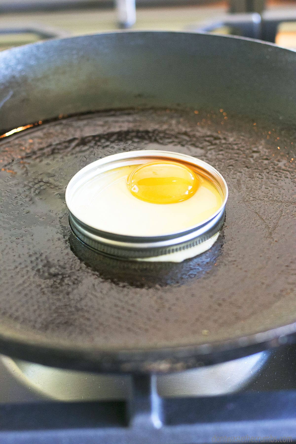 Raw egg in mason jar lid cooking on a skillet.