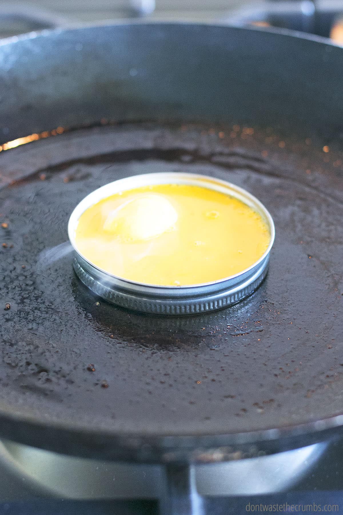 Uncooked egg in a mason jar lid cooking on a skillet.
