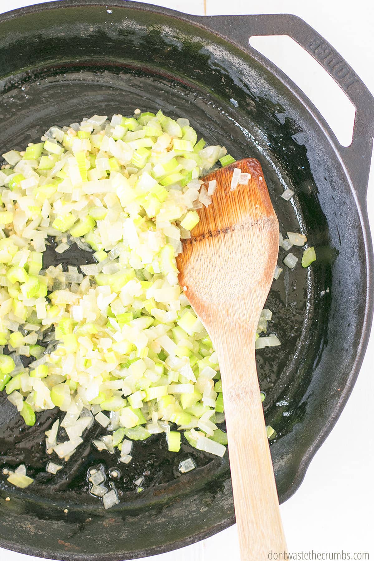 Chopped celery and onion cooking in a cast iron skillet with a wood spoon