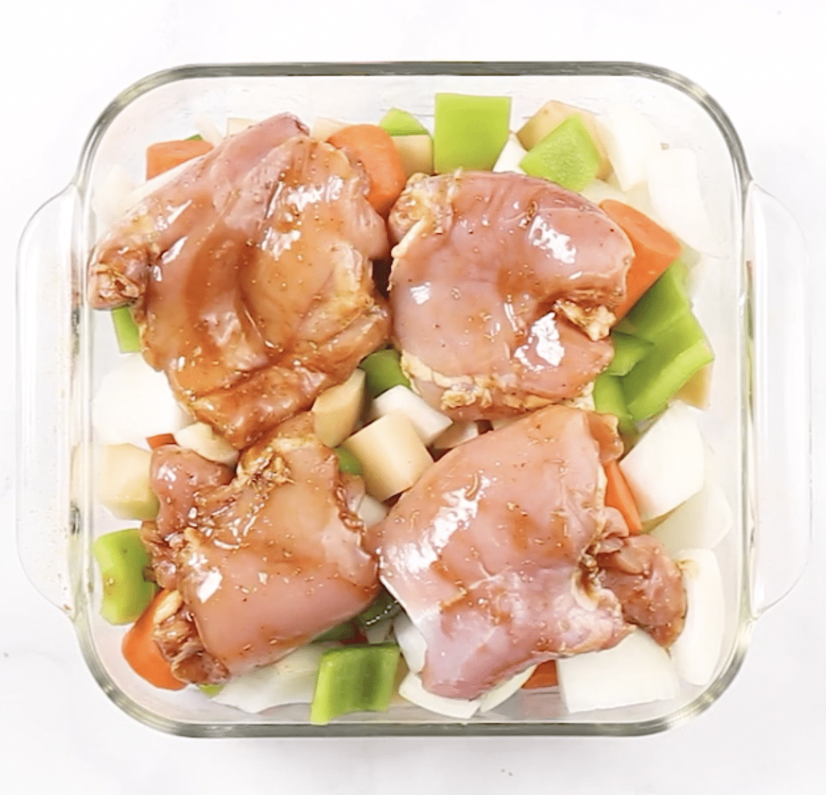 Raw chicken on top of veggies in a glass baking dish