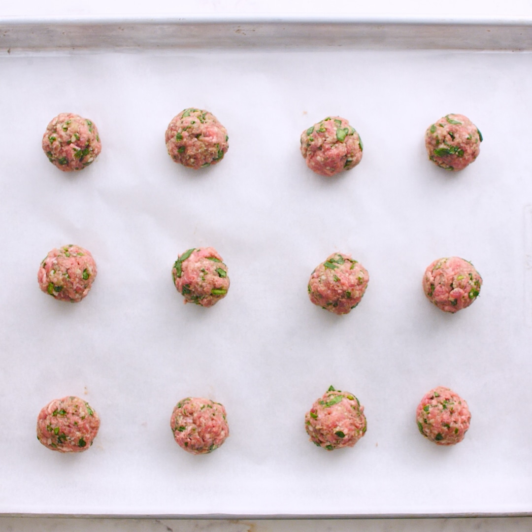 Raw meatballs on a lined baking sheet
