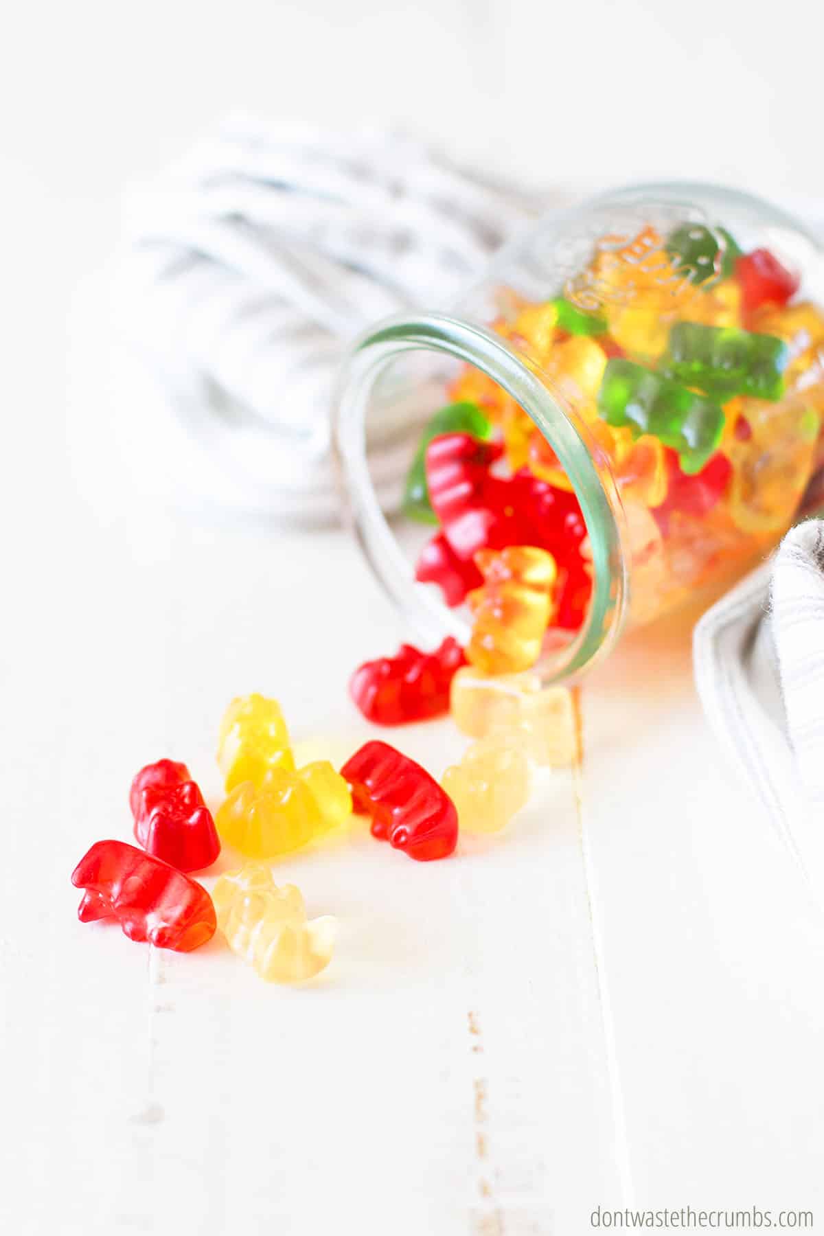 Small glass jar tipped over with gummy bears spilling out onto a counter