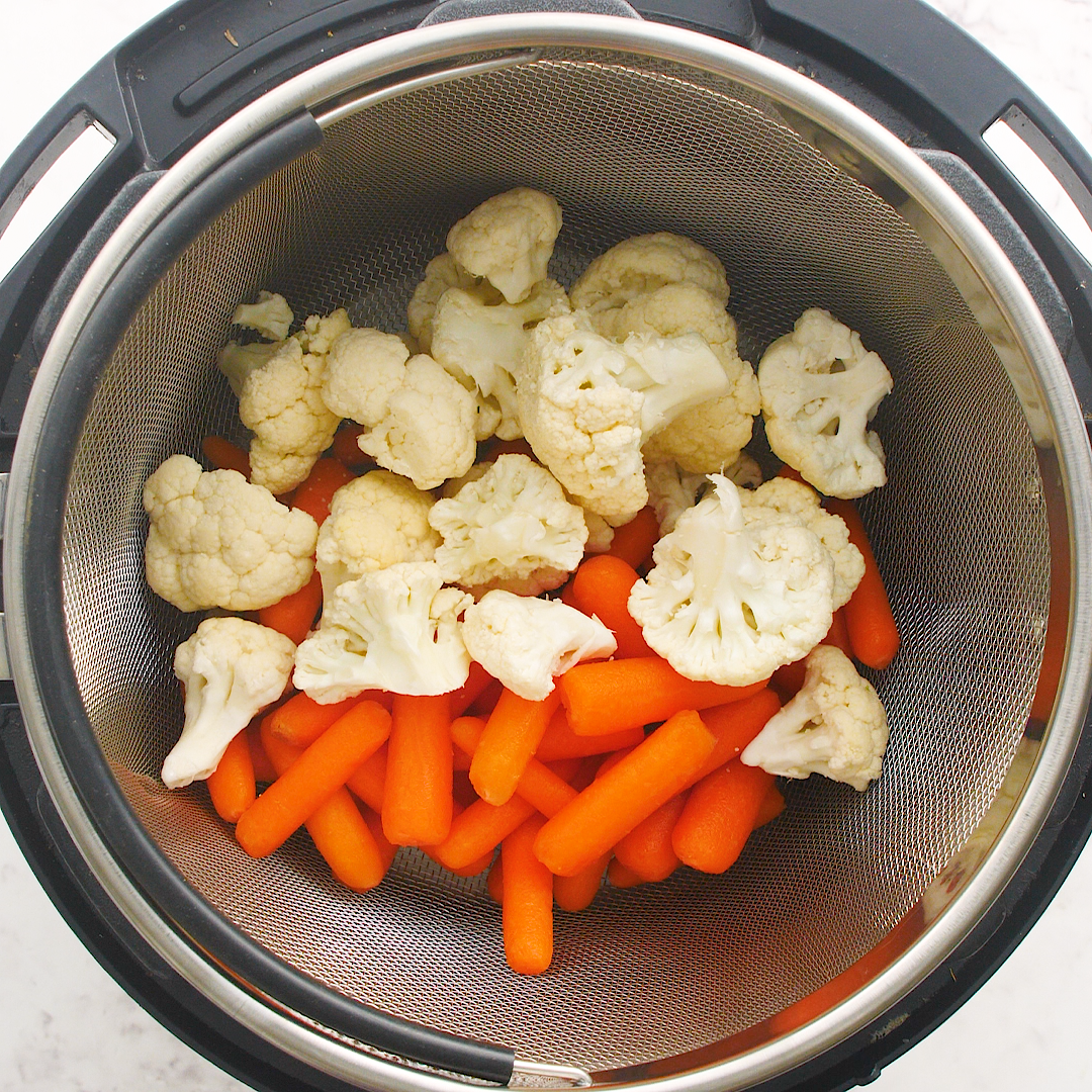 cauliflower and carrots sitting in a steamer basket inside an Instant Pot