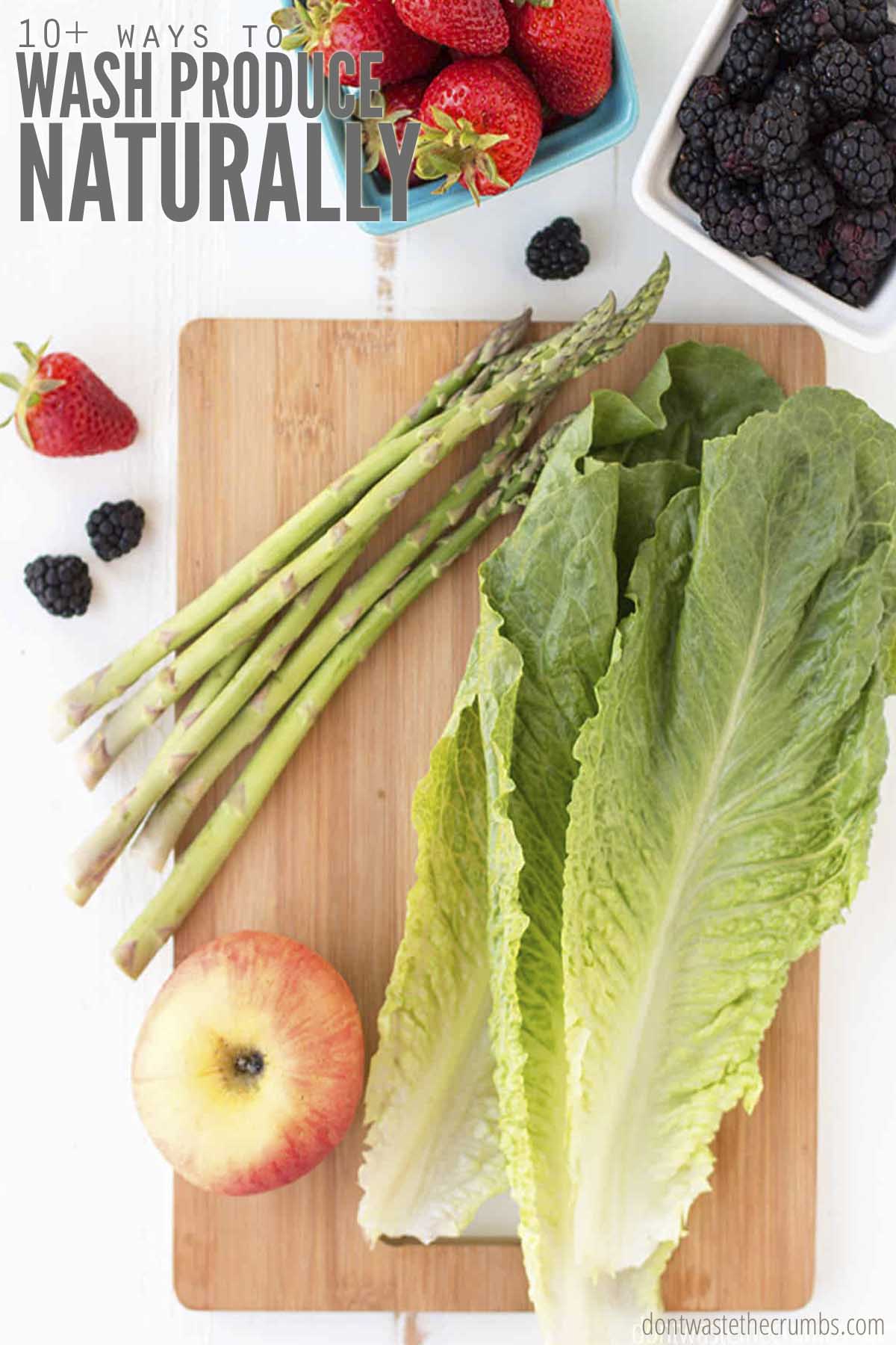 Lettuce and asparagus on a wood cutting board. Two containers of strawberries and blackberries. Text overlay 10+ ways to wash produce naturally.