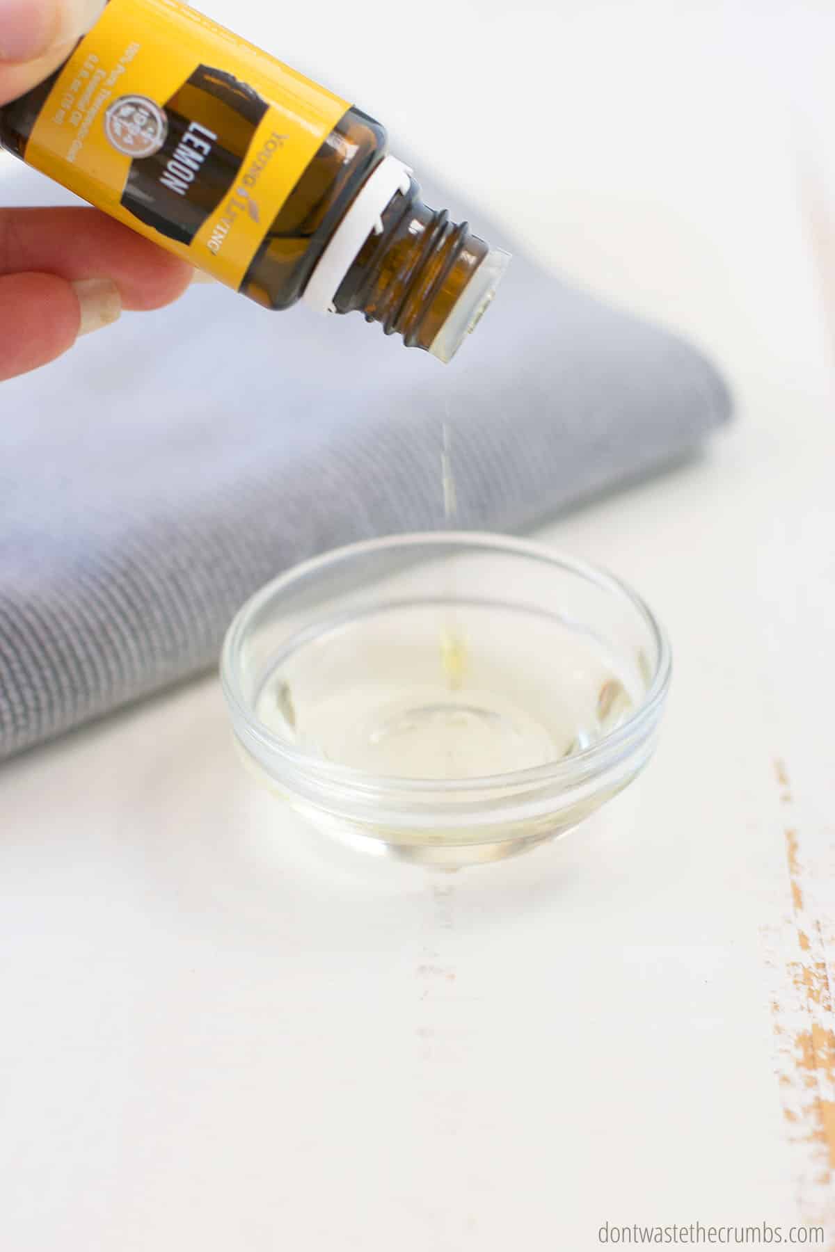 Hand pouring lemon essential oil into a small glass bowl to make wood polish