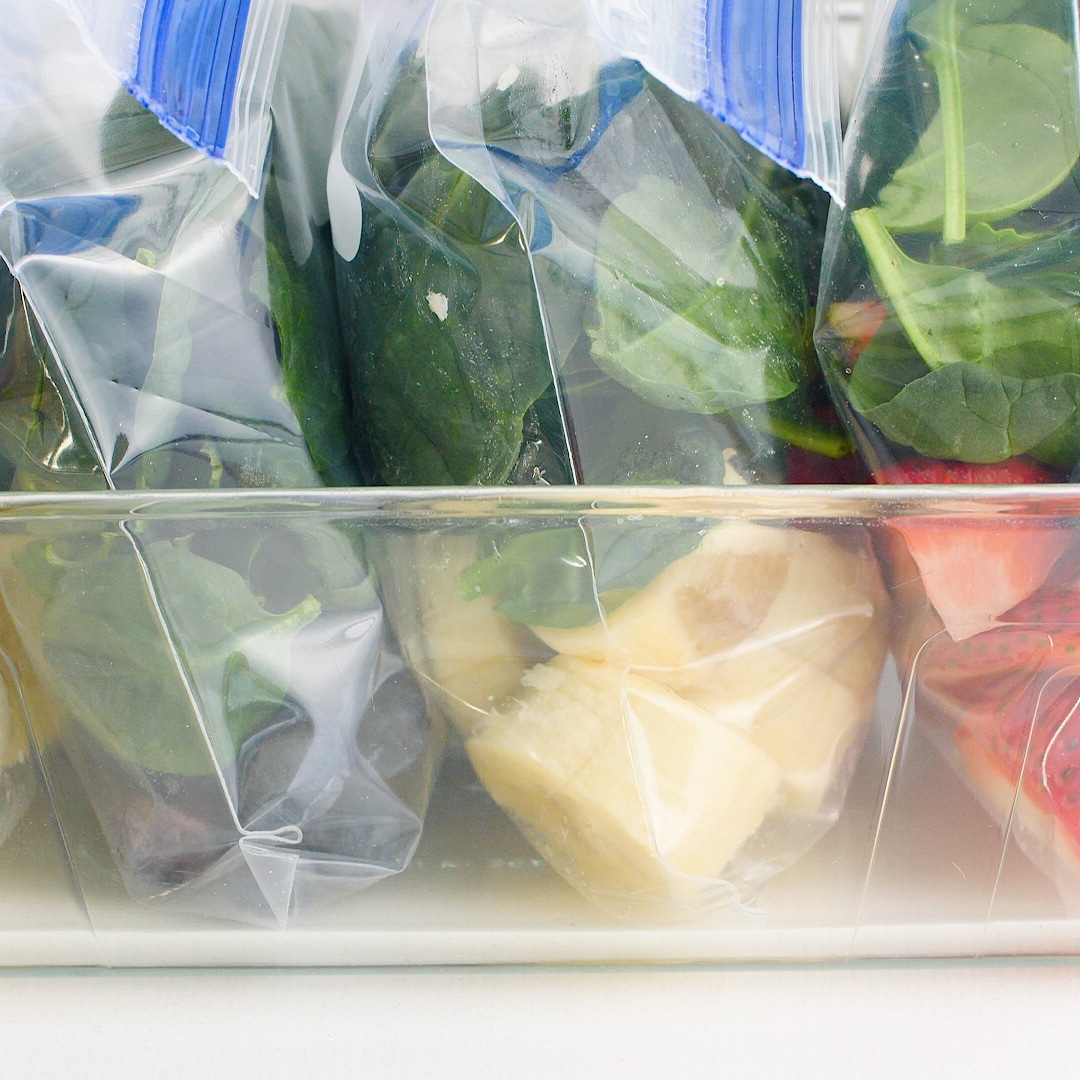 Smoothie packs in ziplock bags lined up in a clear container ready to freeze!
