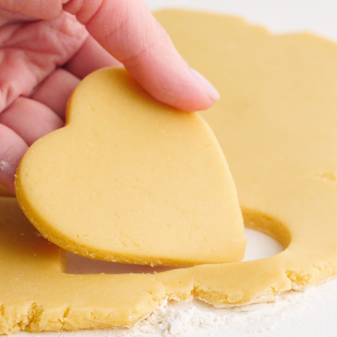 Hand holding a cut out of a heart shaped sugar cookie raw dough