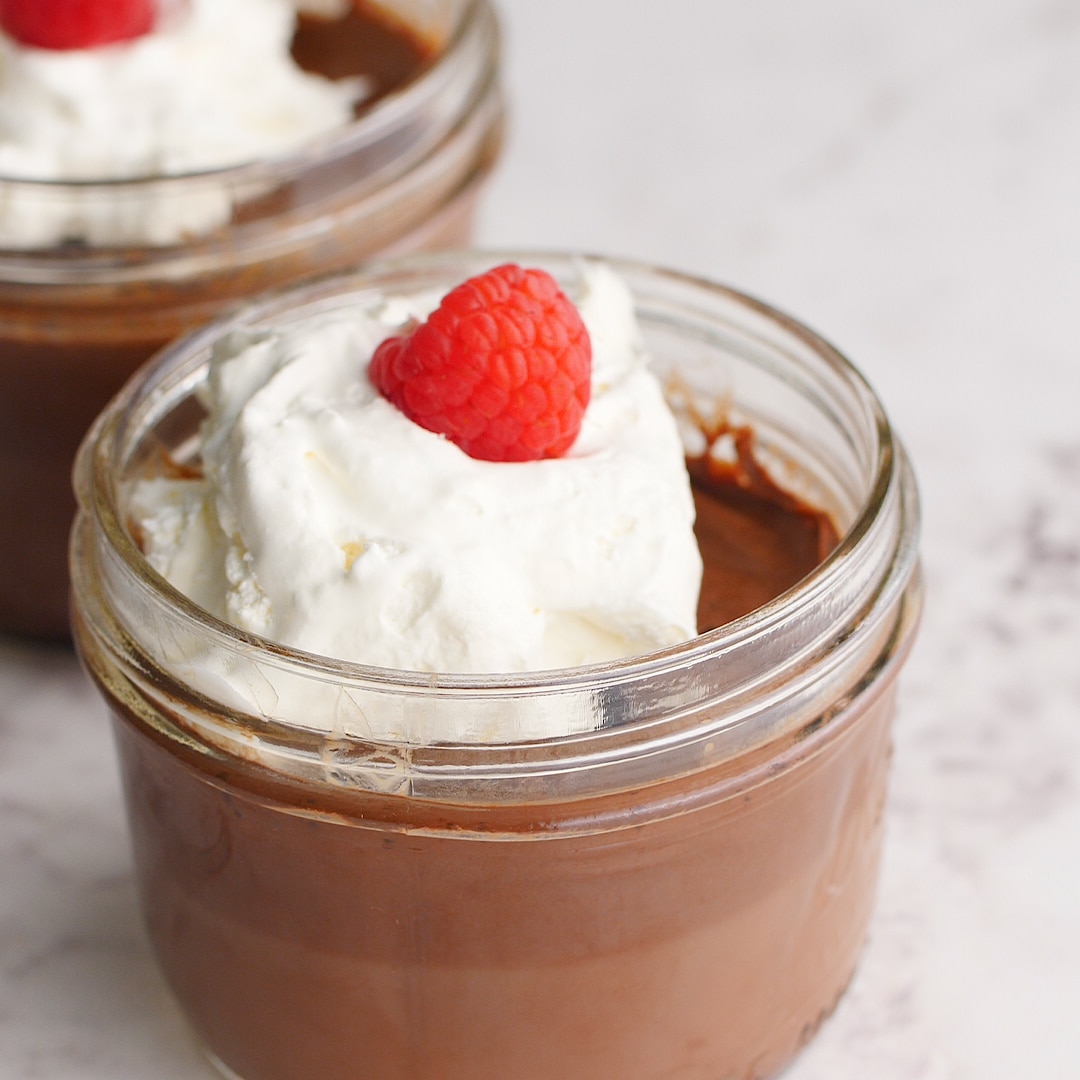 Mason jar full of homemade pudding with whipped cream and a raspberry on top