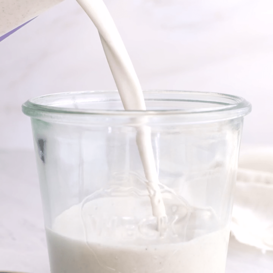 Pitcher of homemade hemp milk pouring into a glass cup