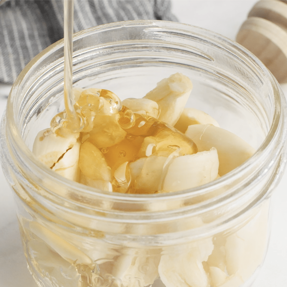 Honey being added to the crushed garlic in a mason jar