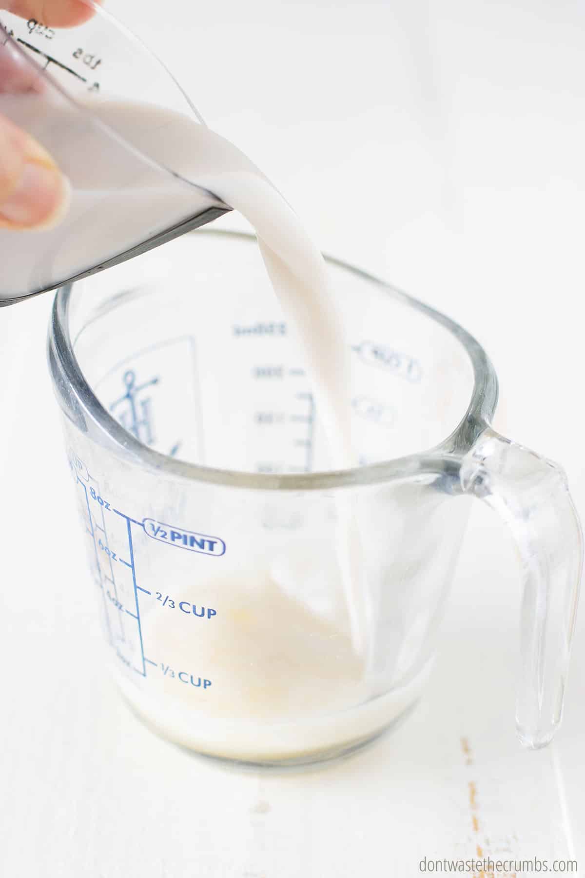 Measuring cup of milk being poured into a measuring cup of lemon juice