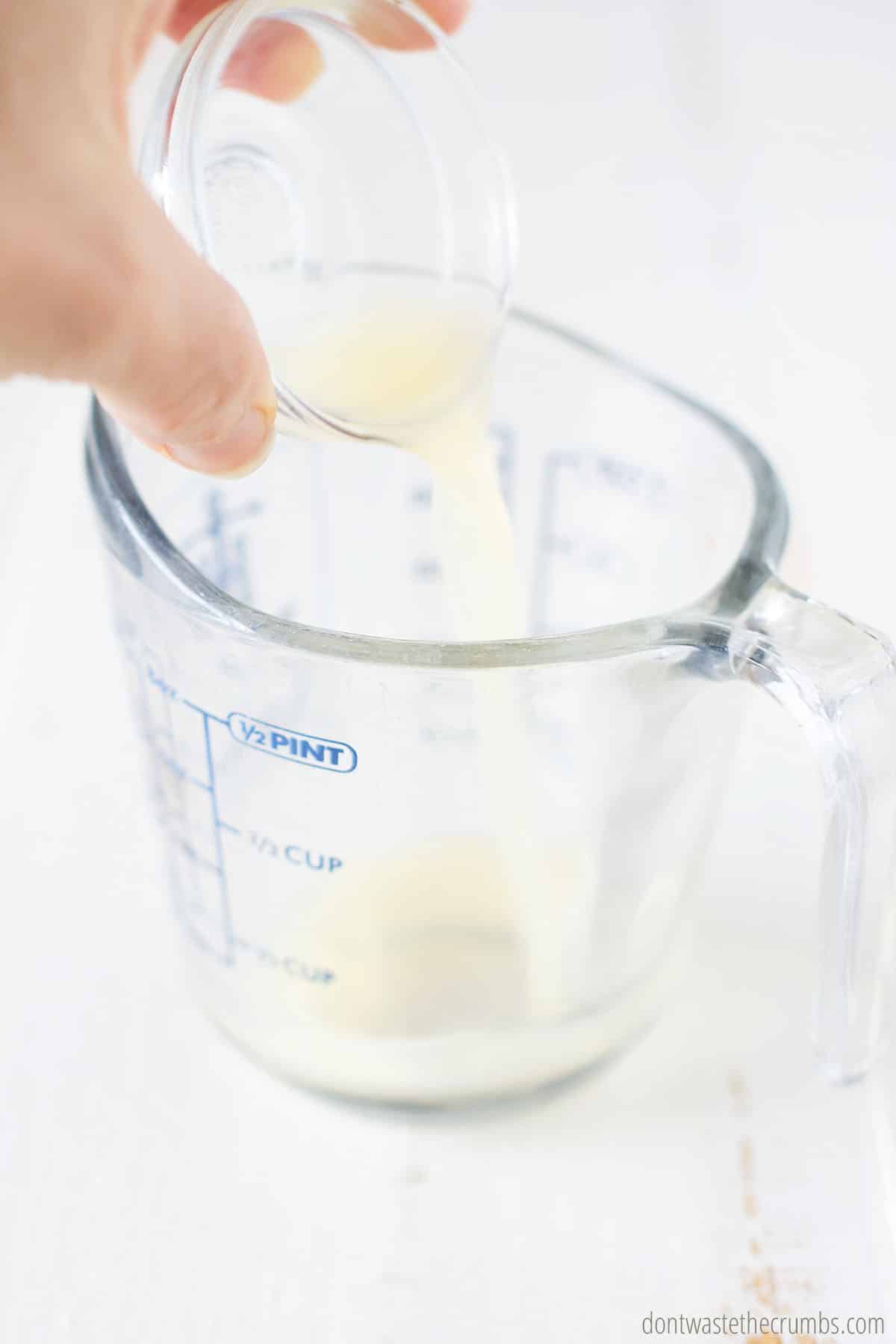 Hand holding a small bowl of lemon juice as it's pouring into a measuring cup
