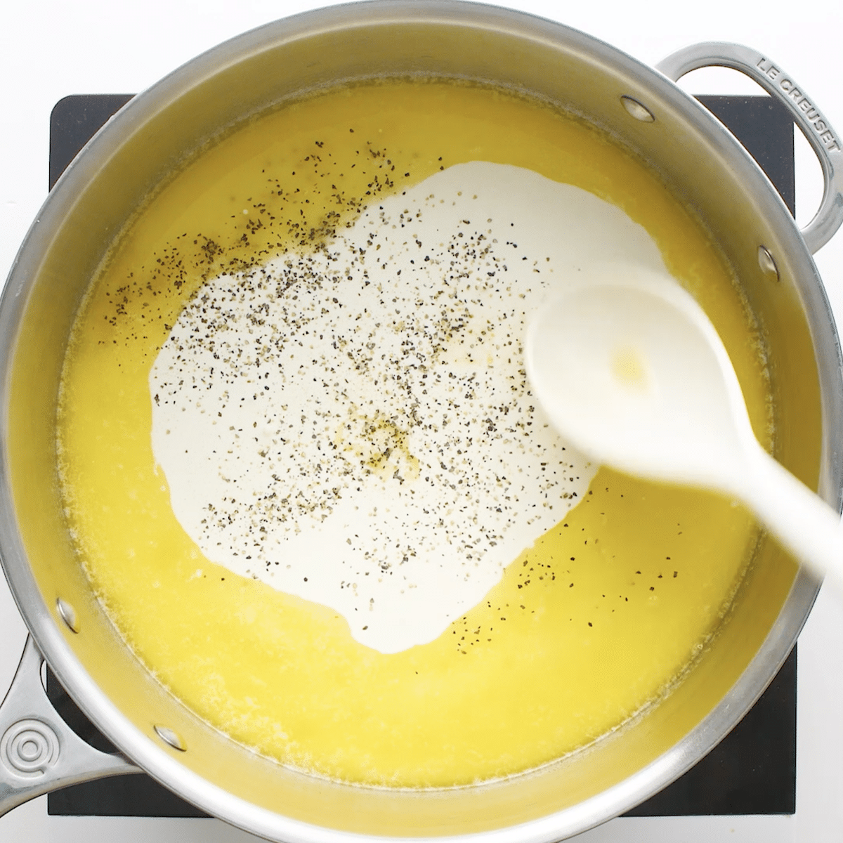 Garlic, heavy cream, butter, and pepper in a sauce pan with a spoon stirring