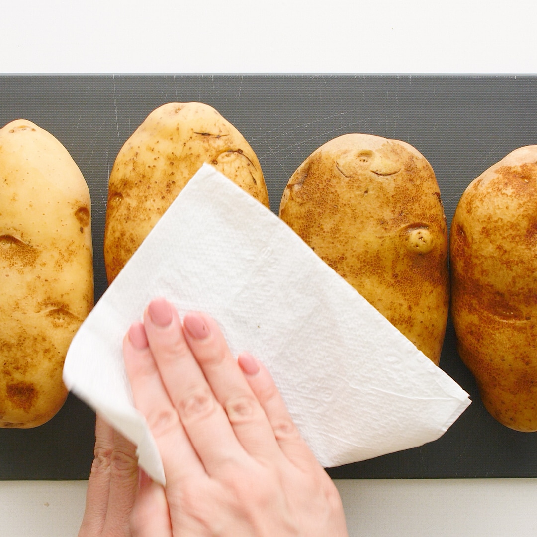 Hand wiping the potatoes clean with a paper towel