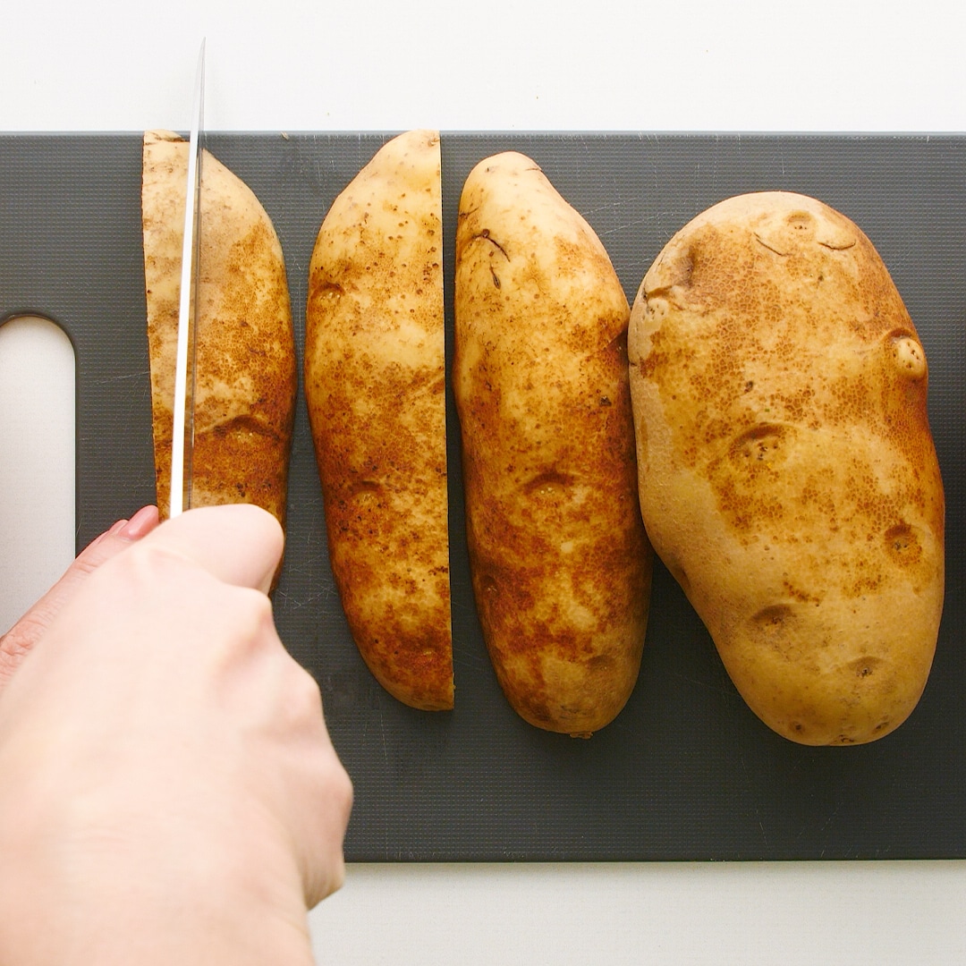Hand slicing potatoes lengthwise with a sharp knife