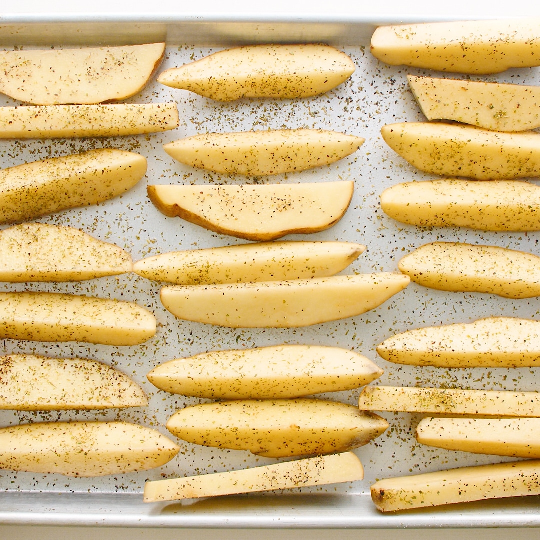 Sliced seasoned potato wedges on a baking sheet