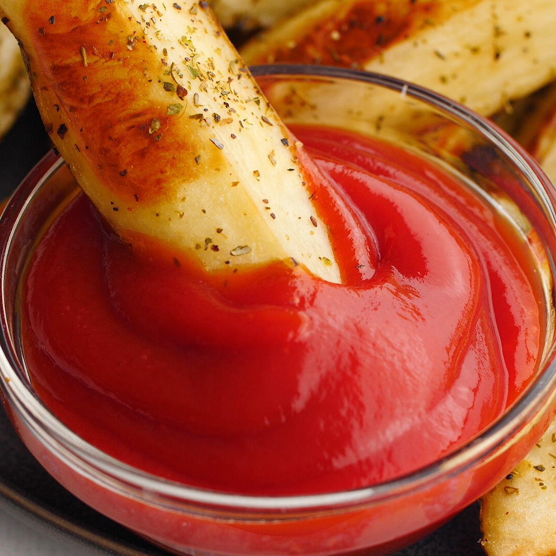 Homemade potato wedge being dipped into a small bowl of ketchup