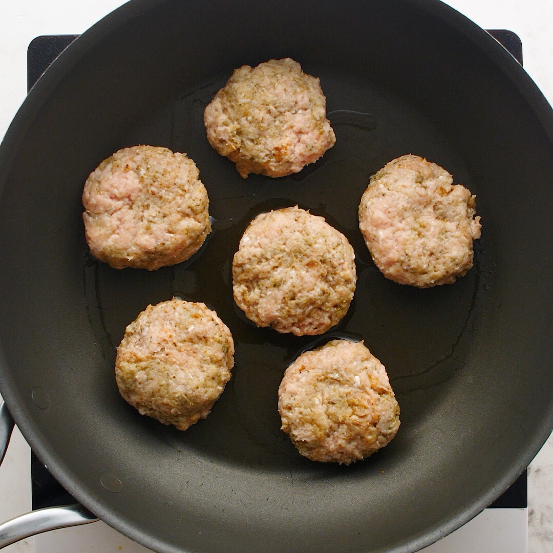 Six sausage patties cooking in a cast iron skillet