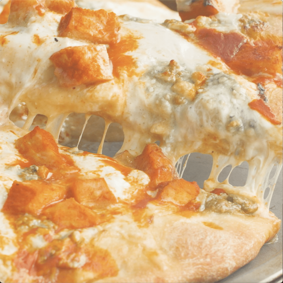 Up close view: Slice of buffalo chicken pizza being lifted from the other slices.