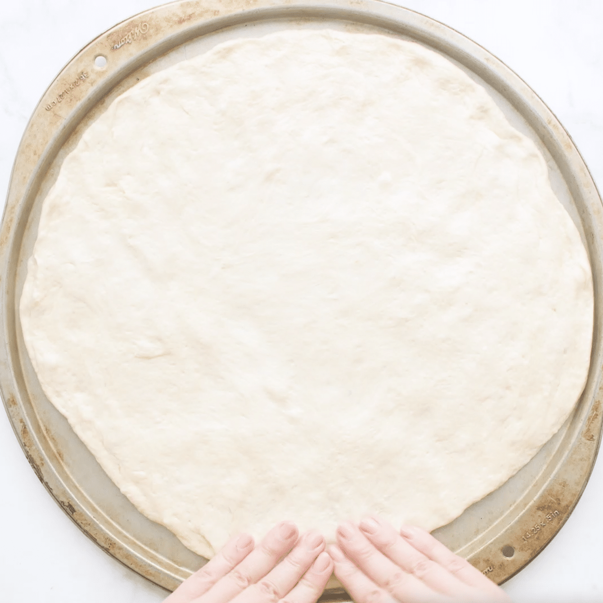 Dough in the shape of a pizza on a pizza stone.