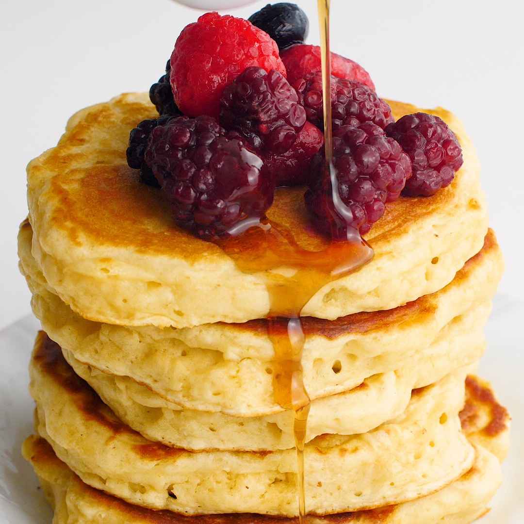 Stack of sourdough pancakes with fresh berries and syrup being poured over the pancakes
