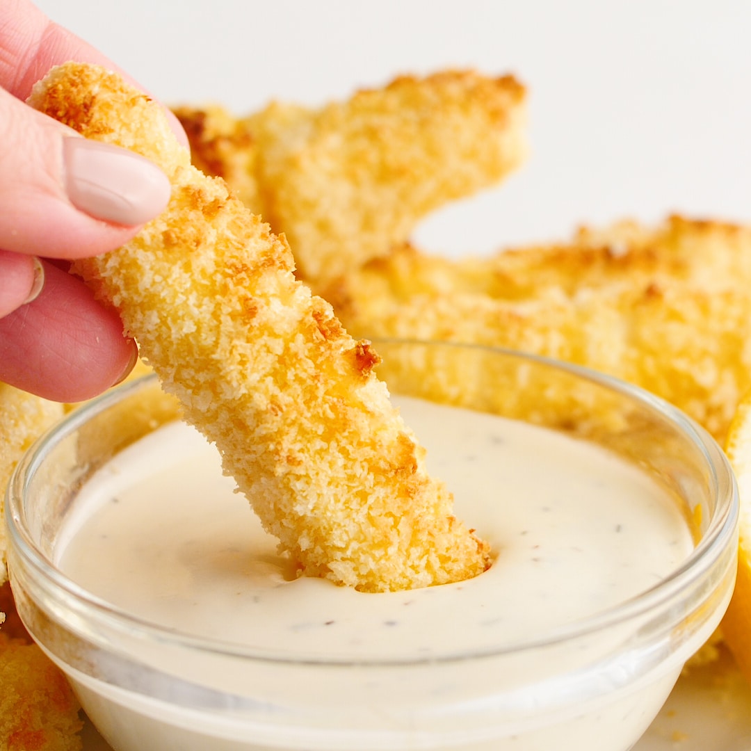 Hand dipping homemade fish fingers into a dip.